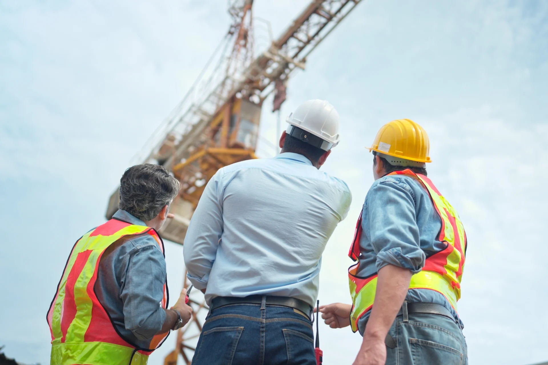 Construction workers wearing safety vests and helmets inspecting a crane at a job site